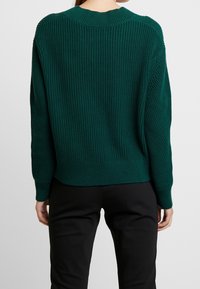 Zielony sweter z dzianiny o prążkowanej fakturze, dopasowanym mankietach i okrągłym dekolcie. Luźny krój z nieco dłuższym tyłem.