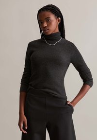 Dark gray ribbed turtleneck sweater with long sleeves, textured fabric, worn with high-waisted black trousers. Simple silver chain necklace.