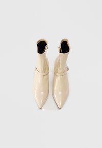 Pair of beige pointed-toe ankle boots with side zippers and thin straps with buckles on a white background.