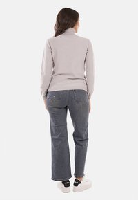 Maglione a collo alto grigio chiaro con una finitura testurizzata, abbinato a jeans dritti grigio scuro e sneakers bianche con dettagli neri.