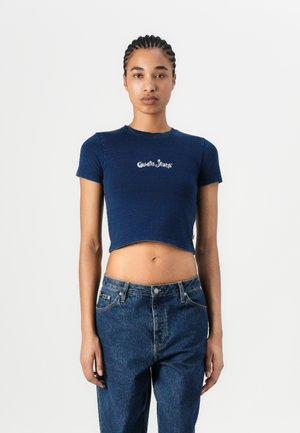 Marineblå crop-top med korte ermer, med hvit brodert "Guess Jeans"-logo på fronten. Mykt, tettsittende materiale.