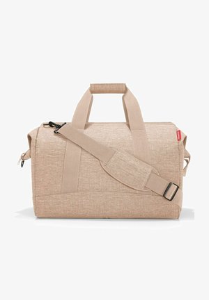 Sac de voyage en tissu beige avec deux poignées supérieures et une bandoulière détachable. Comprend une fermeture à glissière et un matériau texturé.