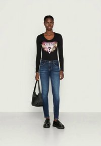 Bodysuit negro de manga larga con gráfico de logo floral, combinado con jeans ajustados azul oscuro. Un bolso negro y unos zapatos gruesos negros completan el look.