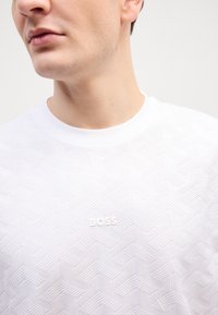 Balts īsām piedurknēm T-krekls ar teksturētu ribiņu rakstu, ar smalku "BOSS" logotipu atbilstošā baltā krāsā uz priekša.