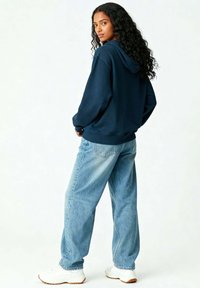 Hoodie bleu marine avec une poche kangourou, associé à un jean bleu clair à coupe ample et des baskets blanches, avec un tissu texturé et des poignets côtelés.