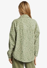 Camisa de pana verde con diseño de estampado de leopardo, que cuenta con cuello de camisa, mangas largas y un corte relajado. Tejido texturizado con detalles de botones.