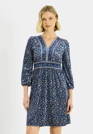 Robe bleue à motif floral avec manches longues bouffantes, col en V et taille cintrée. Présente un motif de feuilles blanches et bleu clair.