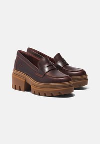 Ruske nahkatoimelised platform loafersi, millel on paks ja robustne tan värvi tallalus, mida rõhutavad kontrastsed oranži õmblused ja dekoratiivne rihm vampi peal.