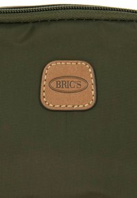 Sacchetto in nylon verde oliva con una patch in pelle marrone con il logo "BRIC'S" a rilievo, chiuso con una zip. Texture liscia.