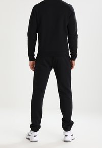 Sudadera de algodón negro y joggers a juego, silueta ajustada, puños y cinturilla de canalé, combinados con zapatillas deportivas blancas.