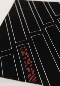 Tissu noir avec des formes géométriques blanches en contour et du texte rouge "onbre" intégré dans le design, présenté sur une surface plane.
