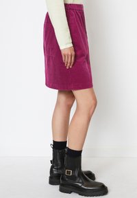 Jupe en velours côtelé rose vif, avec une taille froncée, une poche latérale et une coupe droite. Associée à des bottines noires et des chaussettes.