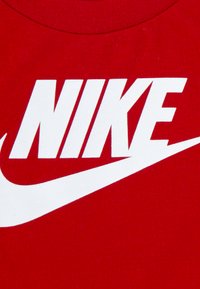 Röd t-shirt med en stor vit "NIKE"-logotyp och en karakteristisk vit swoosh-design, tillverkad av mjukt bomullstyg.