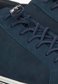 Granatowe zamszowe sneakersy z płaskimi ciemnymi sznurowadłami, srebrnym okuciem i kontrastującymi białymi gumowymi podeszwami. Gładka tekstura z minimalnymi detalami szwów.