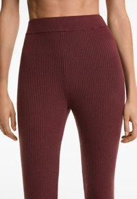 Gerippte Leggings in einem tiefen Burgunderrot mit einem breiten Bund. Der Stoff hat eine weiche Textur und zeigt vertikale Rippungen.