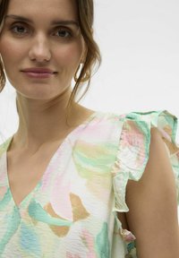 Ziedu raksta tops vieglā audumā, ar V veida kakla izgriezumu un volāniņu piedurknēm pasteļtoņos: rozā, zaļā un bežā.