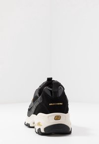 Svart sneaker med texturerat läder och mockamaterial. Har en tjock vit och guldsula, vadderad krage och varumärkesdetaljer på hälen.