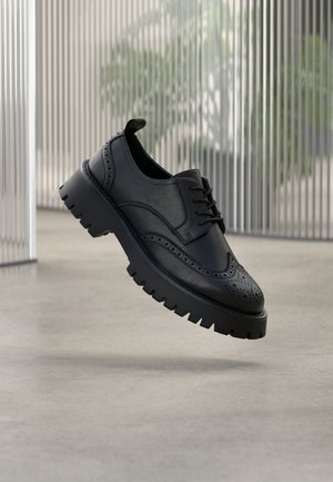 Scarpa brogue in pelle nera con dettagli traforati, suola spessa in gomma e design con lacci. Texture liscia con finitura lucida.