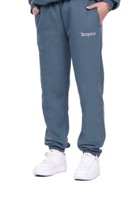 Grå sweatpants med elastiske manchetter og sidelommer; har pink broderet "Dropsize" logo på venstre lår. Parret med hvide sneakers.
