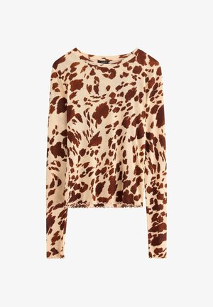Chemise beige à manches longues avec un imprimé animal abstrait marron foncé et des détails en bord « laitue » aux manches et en bas.