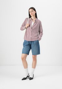 Striped red and white button-up shirt, blue denim shorts, white socks, black heeled shoes, and a light handbag. Simple, casual outfit.