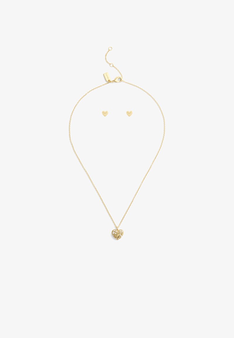 Collar de tono dorado con un colgante en forma de corazón que presenta un grupo de piedras preciosas transparentes, acompañado de pendientes de botón en forma de corazón a juego.