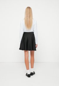 Crna lepršava suknja napravljena od glatkog materijala s srednjom dužinom, uparena s svijetloplavom košuljom dugih rukava i crnim loafericama.