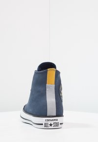 Námořnické modré semišové vysoké tenisky Converse s žlutými a šedými akcenty, logem na patě a bílou gumovou podrážkou s černými pruhy.