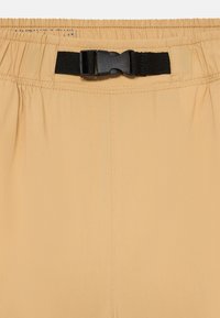 Lys beige shorts med elastisk midje og en svart plastspenne. Glatt tekstur med synlige sømmer og folder.