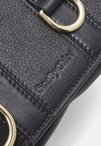 Borsa a mano in pelle nera con superficie testurizzata, hardware in tono oro e logo impresso. Accento circolare notevole sulla tracolla.
