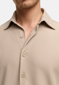 Beige geribde knoop-overhemd met een puntkraag, voorzien van vier knopen en een geweven stof. Ontworpen voor een nauwsluitende pasvorm.