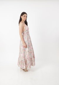 Robe maxi florale avec une base rose pastel clair ornée de motifs de roses et de fleurs bleues, des bretelles spaghetti et un ourlet froncé à volants.