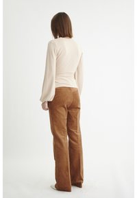 Blusa bege de manga longa com um design ajustado; combinada com calças flared de corduroy castanhas com riscas verticais e um acabamento texturizado.