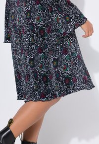 Schwarzes Kleid mit abstrakten weißen, grünen, roten und lila floralem Muster. Fließender Stoff mit plissierter Textur, mit abgerundetem Saum.