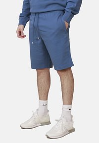 Shorts in cotone misto blu con vita regolabile, tasche laterali e vestibilità rilassata, abbinati a scarpe da ginnastica bianche e calze corte.