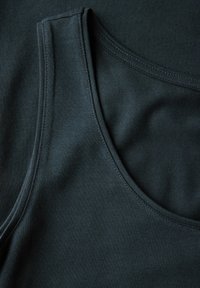 Canotte di cotone verde scuro sovrapposte, caratterizzate da una texture morbida, spalline larghe e cuciture nette lungo il collo e le aperture delle maniche.