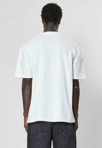 Tricou alb din bumbac, cu mâneci scurte, croi lejer, guler ribat și tiv drept. Purtați cu blugi din denim închis, design minimalist.