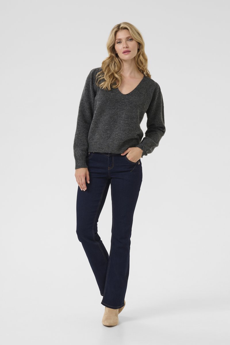 Maglione grigio a scollo a V con maniche lunghe, abbinato a jeans svasati blu scuro. Il modello indossa stivali beige alla caviglia. Texture liscia ovunque.