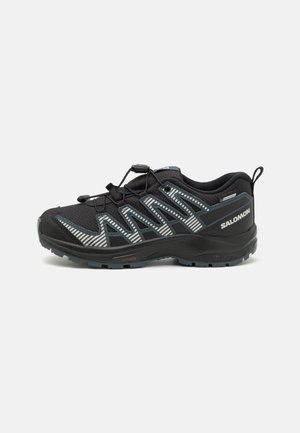 Zapatilla de trail running negra con parte superior de malla transpirable, rayas reflectantes, sistema de cordones elásticos y suela de goma texturizada para mayor agarre.