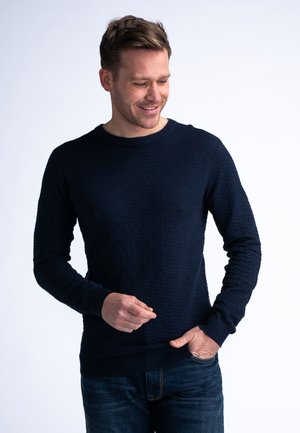Navy blue sweater made of textured fabric with a round neck and long sleeves. Features ribbed cuffs and hem, paired with blue jeans.