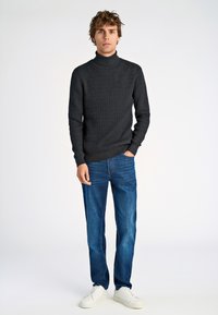 Maglione a collo alto in grigio scuro con texture, abbinato a jeans blu e sneakers bianche. Design semplice e dritto con polsini a coste.
