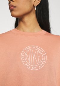 Nike t-shirt i mjuk korallfärgad tyg har en rund logotyp med "NIKE" och "THE SPORTS AND FITNESS COMPANY" i vit brodyr. Korta ärmar.