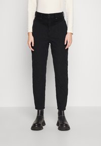 Pantaloni neri trapuntati con vita alta, vestibilità affusolata e motivo a diamante testurizzato. Abbinati a stivali alla caviglia.