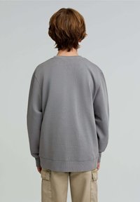 Felpa grigia in cotone con colletto rotondo, texture a coste e maniche lunghe, indossata con pantaloni cargo beige.