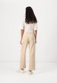 Beige corduroy cargo pants with a relaxed fit, featuring side and back pockets, and a fabric patch on the back pocket.