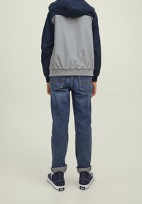 Grå och marinblå huvjacka med elastisk nederkant, tillsammans med blå denimjeans och marinblå sneakers. Synlig sömnad på jeansen, avslappnad passform.