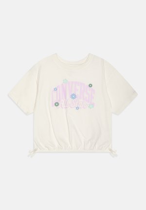 T-shirt accorciato di colore crema, realizzato in cotone, con una grafica floreale che presenta la scritta “CONVERSE All Star” in colori pastello e un orlo regolabile con cordoncino.