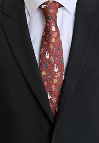 Cravatta rossa decorata con pupazzi di neve, omini di pan di zenzero, decorazioni e regali su uno sfondo a pois; indossata con una camicia bianca e una giacca nera.