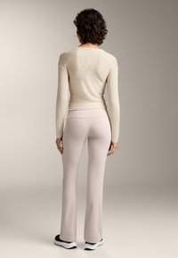 Beiger, gerippter Langarmoberteil und hellpinke, ausgestellte Leggings. Das Oberteil hat eine horizontale Textur und enganliegende Ärmel; die Leggings haben eine glatte Oberfläche.