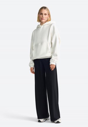 Weiße Kapuzenjacke mit einer Tasche auf der Vorderseite, kombiniert mit schwarzen weit geschnittenen Hosen und weißen Sneakers. Glatte Textur, lässige Passform.